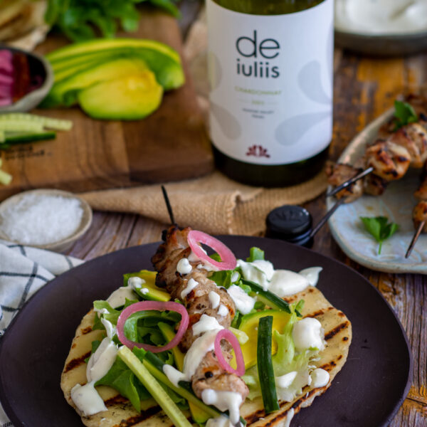 A bottle of chardonnay sits paired next to a delicious meal of greek style chicken skewers and homemade flatbread